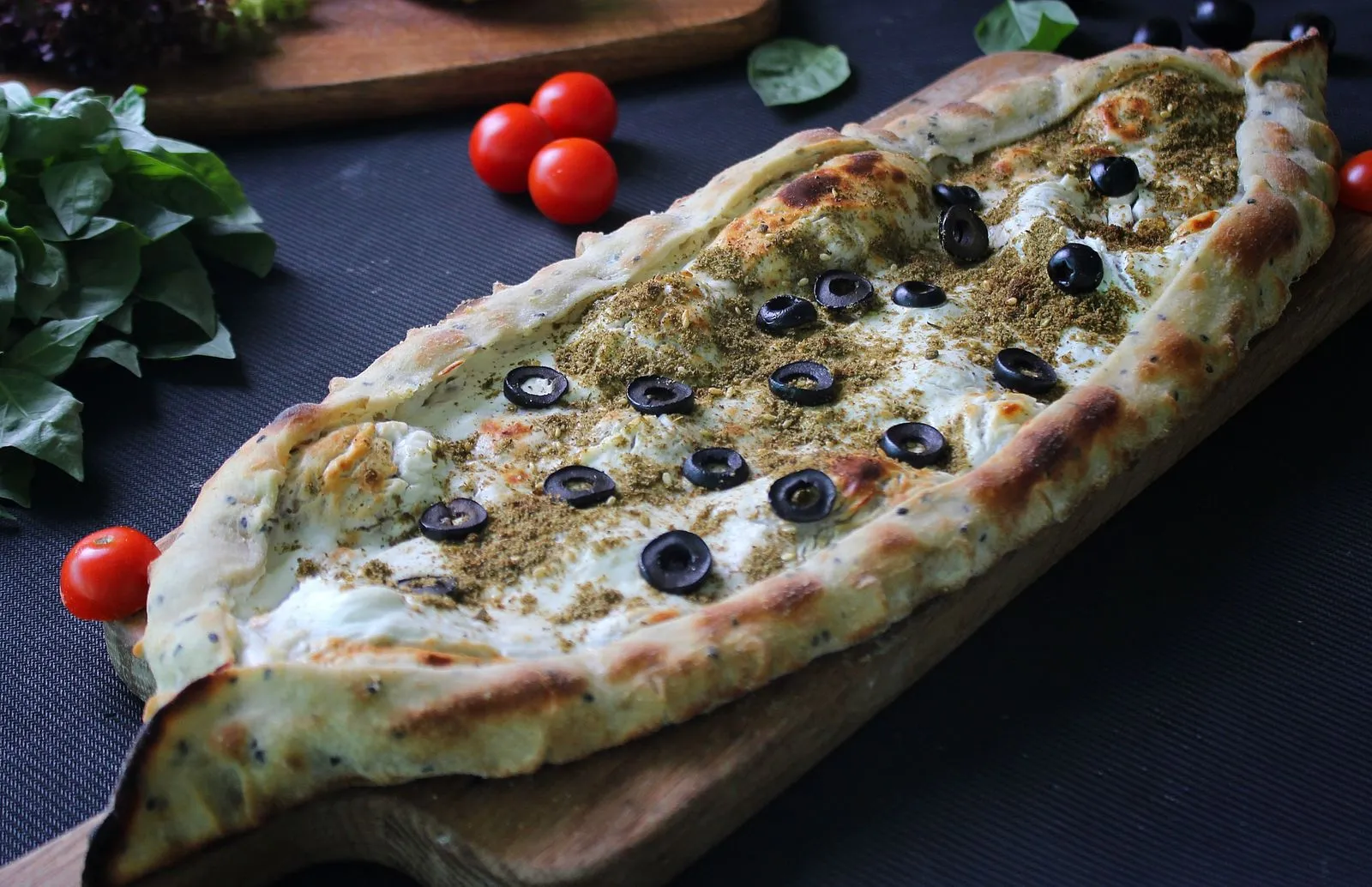 Delicious Middle Eastern flatbread topped with herbs and olives on a wooden board.